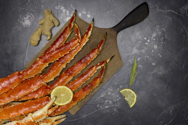 Fresh king kamchatka crab\'s claw with lemon slices, ginger and rosemary at wooden board on black background