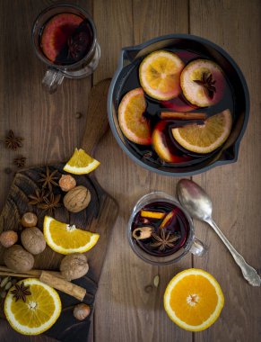 Mulled şarap cam, şarap, portakal, ceviz, fındık, kaşık ve ahşap arka plan, yakınındaki baharatlar ile pan