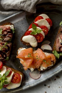 Sığır eti ve roka, somon ve kimyon, mozzarella ve domates kahverengi ekmek gri plaka üzerinde sandviç ile kızartma