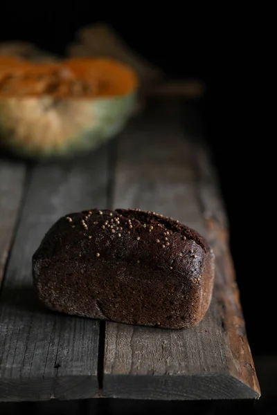 Black grain bread with pumpkin at table on dark background