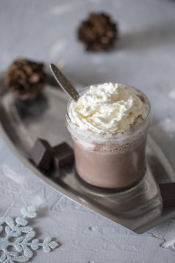 Cam metal tepsi kaşık, siyah fener, yılbaşı çelengi, koni ve dilim koyu çikolata, gri beton zemin üzerinde kremalı tatlı lezzetli sıcak çikolata. Noel kompozisyon.