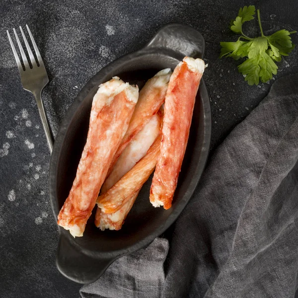 Luxury kamchatka\'s crab sticks on black plate with parsley, fork and napkin at black background. Holiday dish