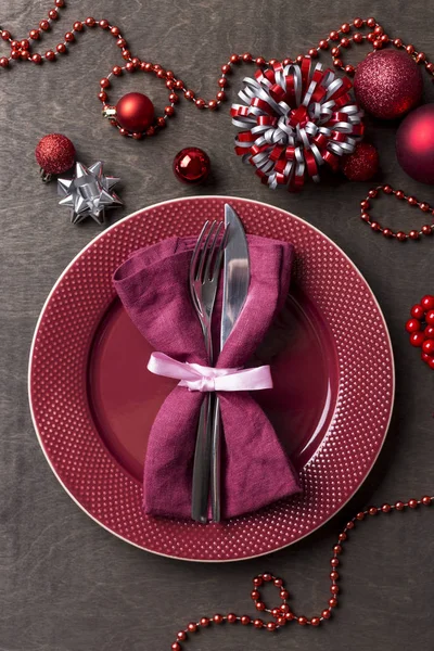 Top view of red serving plate setting on wood table for christmas eve or new year\'s dinner. Red plate, fork, knife, red napkin and festive decor near