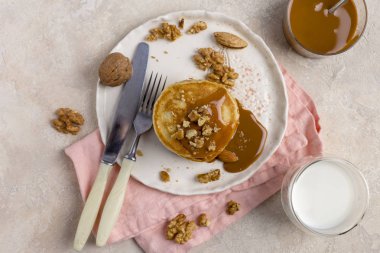 Haşlanmış yoğunlaştırılmış süt ve ceviz, badem çatal, bıçak, pembe peçete, karamel ve süt, açık renkli cam kavanoz ile beyaz tabakta ile pişmiş krep yığını. Romantik yemek, Kahvaltı