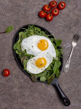 Kahverengi zemin, sağlıklı bir yaşam tarzı kavramı üzerine çatal ile iki kızarmış yumurta Pan otlar, roka, ıspanak, pazı ve kiraz domates, farklı tür. Kahvaltı, üstten görünüm