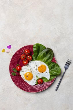 İki kızarmış yumurta, domates, salata ile romantik kahvaltı romano kırmızı plaka, kalp şeklinde sopa, çatal yakınındaki açık renkli. Dikey boş alan, üstten görünüm şablonu.