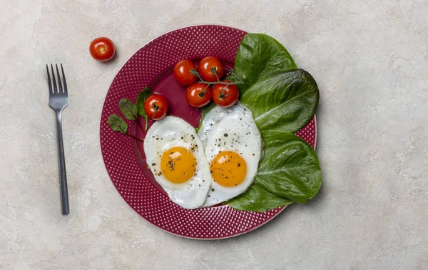 心形的两个煎蛋与罗马诺沙拉和樱桃西红柿在红色盘子与叉子在白色背景 意大利健康食品的横向概念 — 图库照片