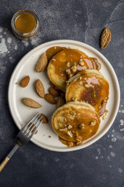 Koyu arka plan üzerinde çatal ile karamel ve fındık beyaz plaka ile yakın çekim taze Amerikan krep. Makro. Tatlı gıda kavramı