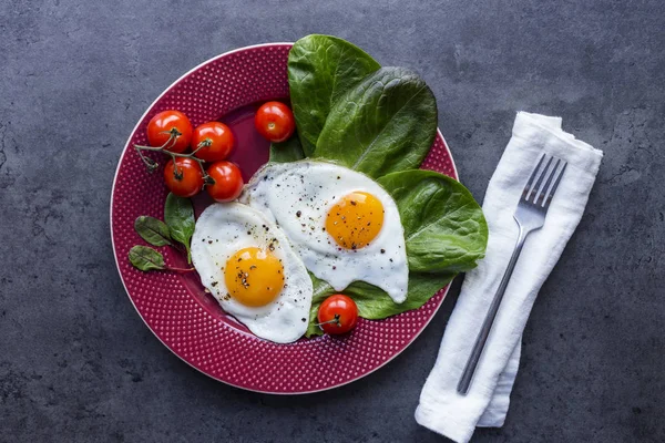 Serving plate with fried eggs, salad and tomatoes, fork and napkin at black background. View from above, cover for magazine