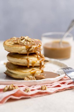 Karamel ve ceviz ile pembe peçete, çatal ışık arka plan üzerinde beyaz tabakta krep yığını