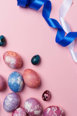 Pembe bir arka plan üzerinde beyaz ve mavi kurdele ile şenlikli Paskalya yumurtaları