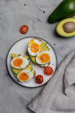 Tahıl ekmek haşlanmış yumurta ve gri arka plan üzerinde plaka üzerinde avokado ile Burger
