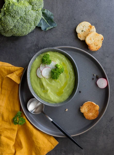 Broccoli soup with toast and raw broccoli and spoon on gray background