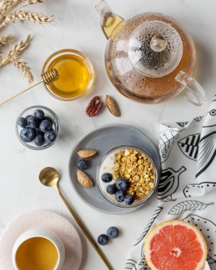 Beyaz mermer arka plan üzerinde çay, bal ve greyfurt ile yaban mersini ile kavanozda Granola