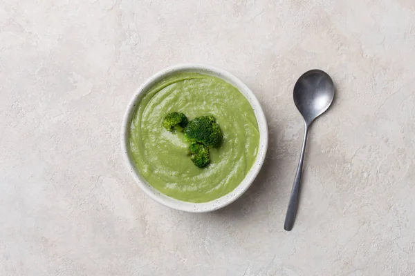 Cream soup with broccoli in white dish with spoon on white concrete background — Stock Image Cream soup with broccoli in white dish with spoon on white concrete background Royalty Free Stock Images