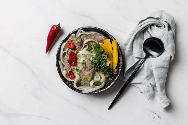 Asian soup with noodle, beef and vegetables in bowl with napkin on white background with black spoon — Stock Photo, Image