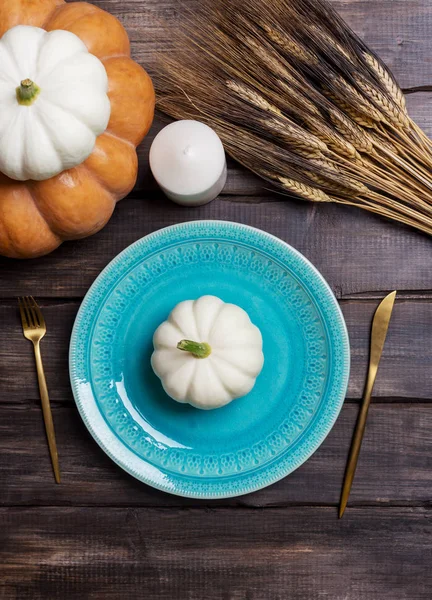 Голубая сервировочная тарелка с белым кабачком на ней, золотая посуда, свеча и пшеница на деревянном фоне — стоковое фото