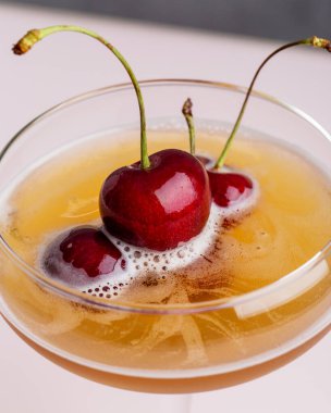 Pembe arka planda kirazlı makro kokteyli kapat. Tatlı kiraz meyveleri köpüklü içecekler şampanya bardağında yumuşak pembe katı arka planda.