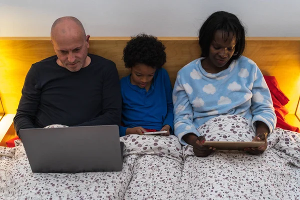 interracial family using portable devices in bed