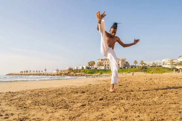 Young brazilian in white pants practicing capoeira (brazilian martial art that combines elements of dance, acrobatics and music) on the beach