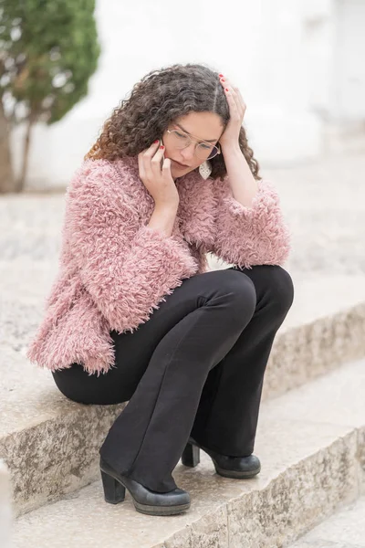 Young beautiful woman sitting in the city park and talking worried on the phone