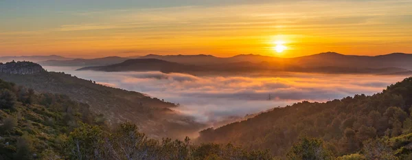 Panoramic view of dawn above the sea of fog. Fantastic sunset in the mountains landscape with sunny beams
