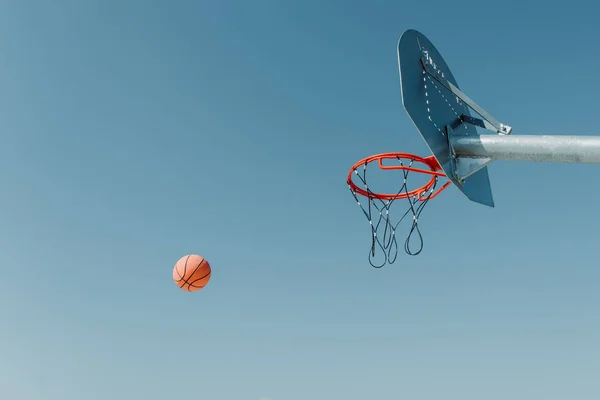 Metal street basketball board with hoop on outdoor court against blue sunny sky. Copy space