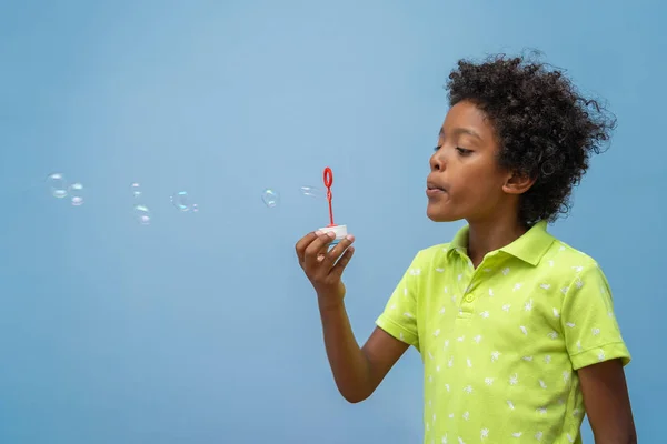 little black boy blowing soap bubbles on blue background, lateral view