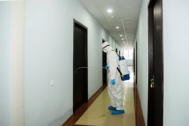 Virüs koruyucu giysiler giyen ve koronavirüs binalarını spreyle dezenfekte eden insanlar.