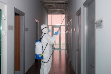 Virüs koruyucu giysiler giyen ve koronavirüs binalarını spreyle dezenfekte eden insanlar.