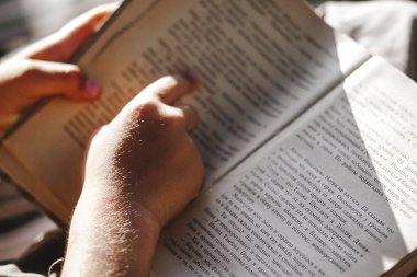 Bahçede bir salıncak üzerinde ilginç bir sanat kitabı okuyan bir çocuğun elleri