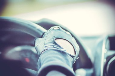 Arabanın direksiyonunda deri eldivenli genç bir sürücünün eli.