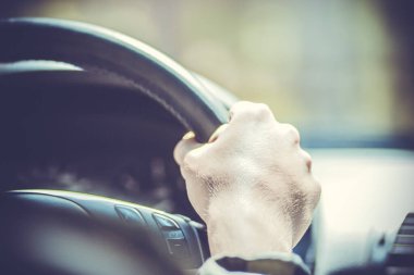 Genç bir adamın eli arabanın direksiyonunda ön camın önünde.