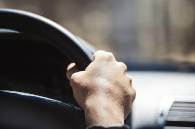 Genç bir adamın eli arabanın direksiyonunda ön camın önünde.