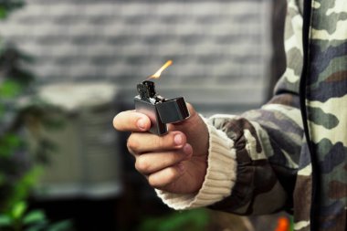 Genç bir adamın ellerinde yanan metal çakmak.