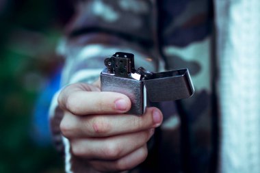 Genç bir adamın ellerinde yanan metal çakmak.