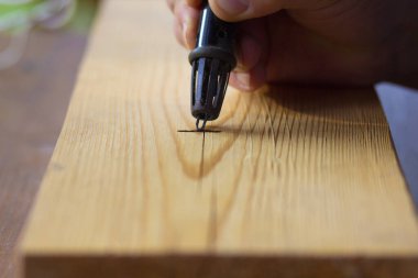 Tahta üzerinde bir insanın elindeki elektrikli ocağın iğnesi.