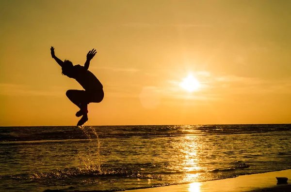 The silhouette of a man in a jumping position In the sea at sunset The idea may be used as a background or wallpaper.