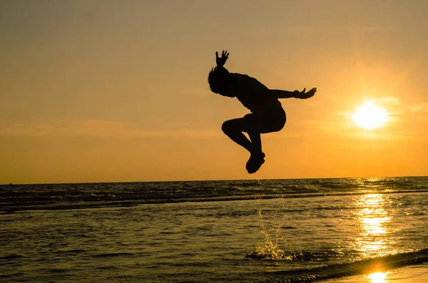 Gün batımında denizde zıplama pozisyonunda bir adamın silueti Fikir bir arka plan veya duvar kağıdı olarak kullanılabilir.