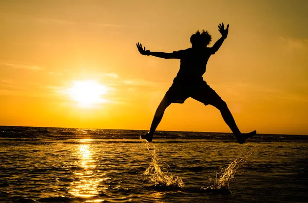 The silhouette of a man in a jumping position In the sea at sunset The idea may be used as a background or wallpaper.