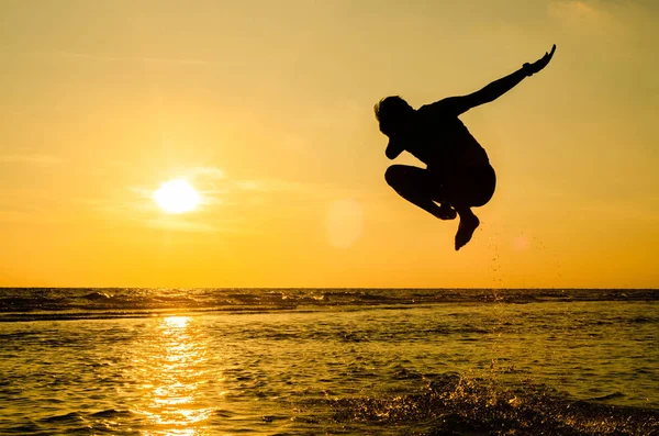 Gün batımında denizde zıplama pozisyonunda bir adamın silueti Fikir bir arka plan veya duvar kağıdı olarak kullanılabilir.