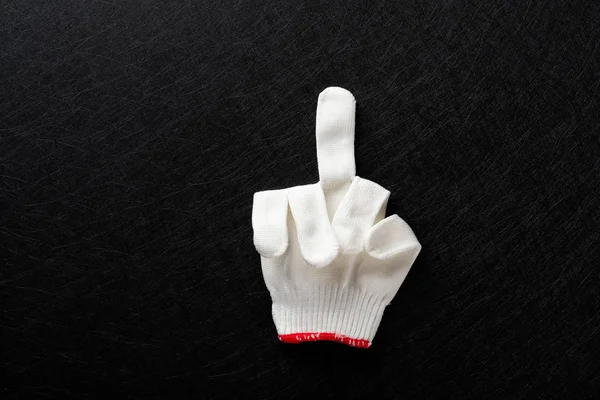 an offensive gesture of middle finger up made by white glove on black background