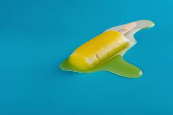 side view yellow popsicle in a melting process on blue background