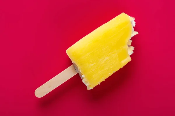 yellow popsicle with some bites on a rose red background