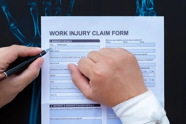 filling up a work injury claim form with a wrapped hand on top of an X-ray film medical and insurance concept