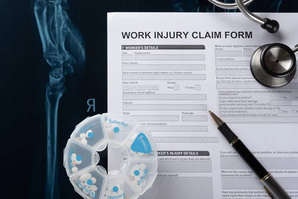 work injury claim form with stethoscope  and box of pills on top of an X-ray film medical and insurance concept