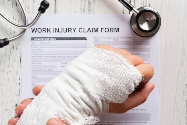 Man Holding His Wrapped Hand Top Work Injury Claim Form — Stock Photo, Image