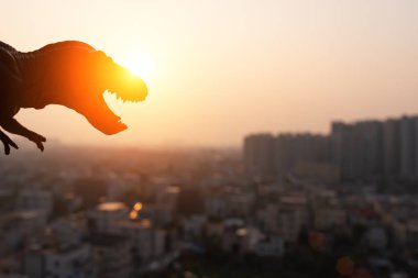 Silhouette tyrannosaurus ve günbatımı zamanı binalarda