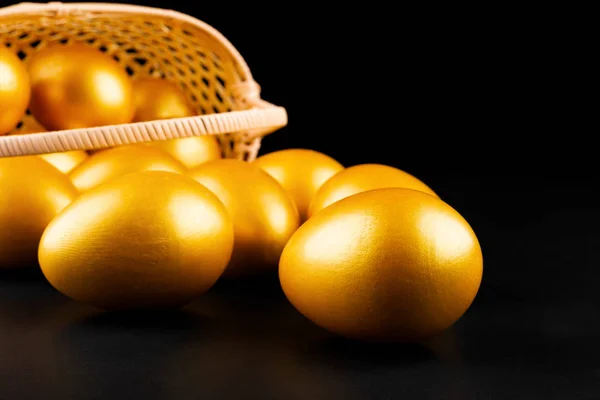 gold eggs rolling out from a basket on black background