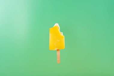 yellow popsicle with some bites on a light green background clipart